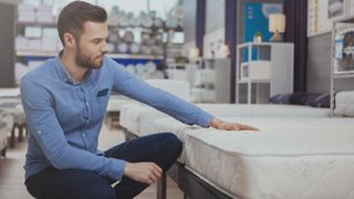 A man in a blue shirt goes mattress shopping