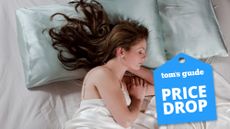 A woman with long dark hair sleeps on new silk bed sheets. A blue price drop sales badge is overlaid in the bottom right corner